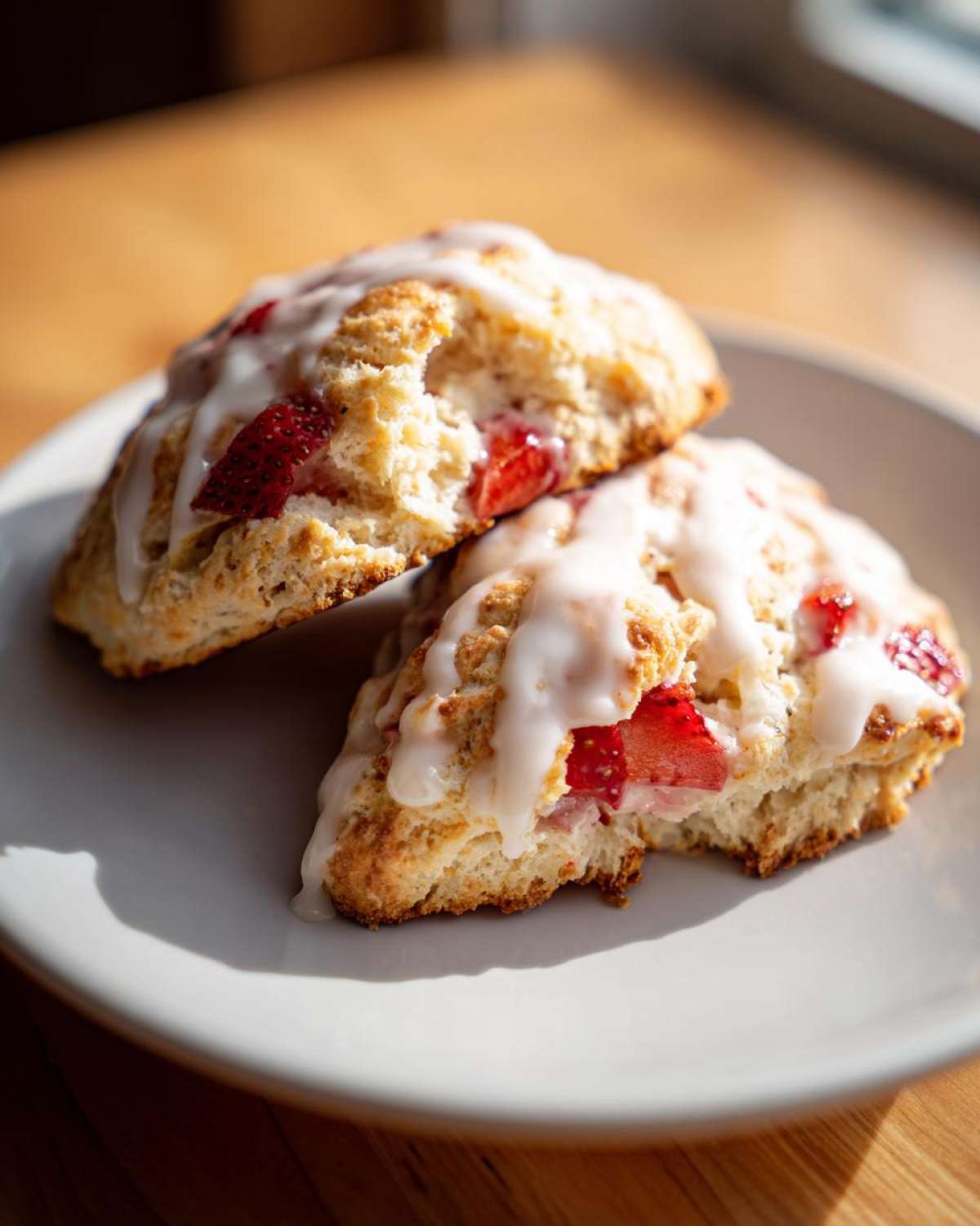 Close-up of two delicious Strawberry Cream Scones with Vanilla Glaze drizzled over fresh strawberries.