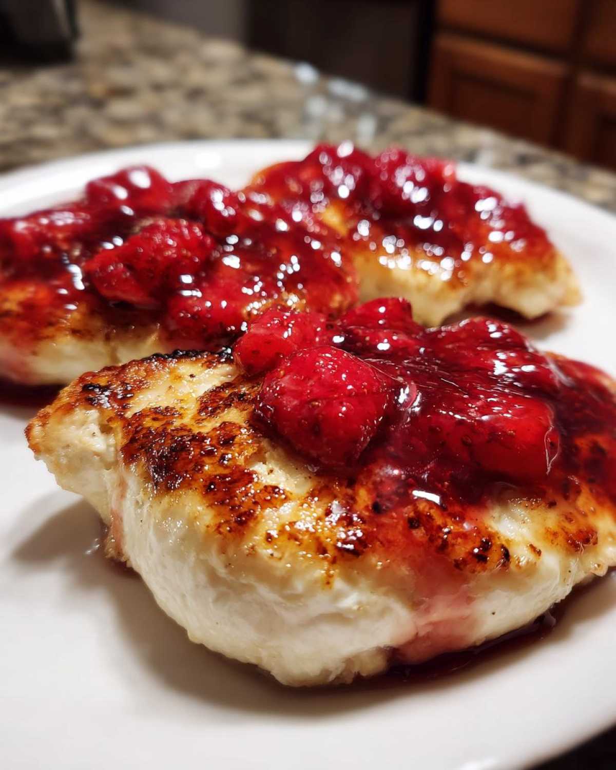 Close-up of two seared Strawberry Goat Cheese Chicken Cutlets topped with a glistening, chunky strawberry sauce.