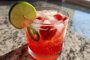 Close-up of a bright red Strawberry Jalapeno Margarita Mocktail filled with ice, strawberries, and a lime wedge garnish.