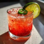 Close-up of a vibrant red Strawberry Jalapeno Margarita Mocktail over ice, garnished with a lime wheel and a jalapeño slice.