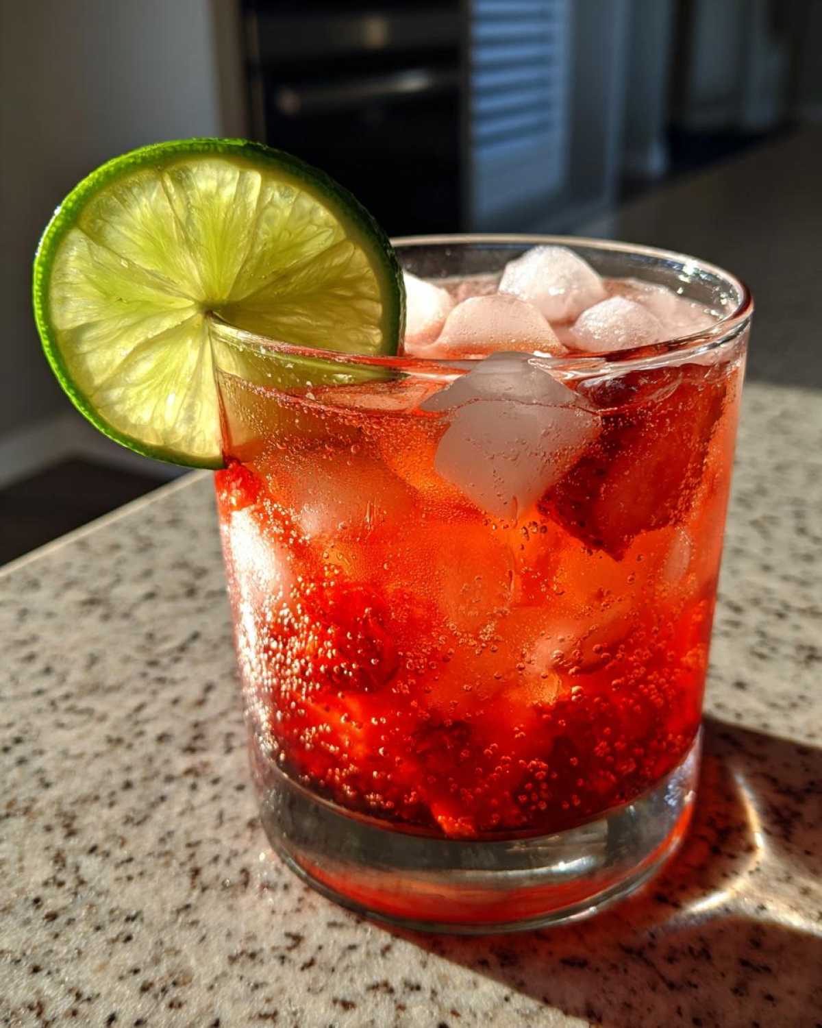 Close-up of a vibrant red Strawberry Jalapeno Margarita Mocktail filled with ice and garnished with a fresh lime wheel.