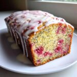 Close-up of a slice of Strawberry Lemon Poppyseed Loaf showing bright pink fruit, poppy seeds, and a thick lemon glaze.