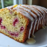 A close-up of a slice of Strawberry Lemon Poppyseed Loaf, showing the moist crumb, poppy seeds, and bright red strawberries, topped with a thick white glaze.