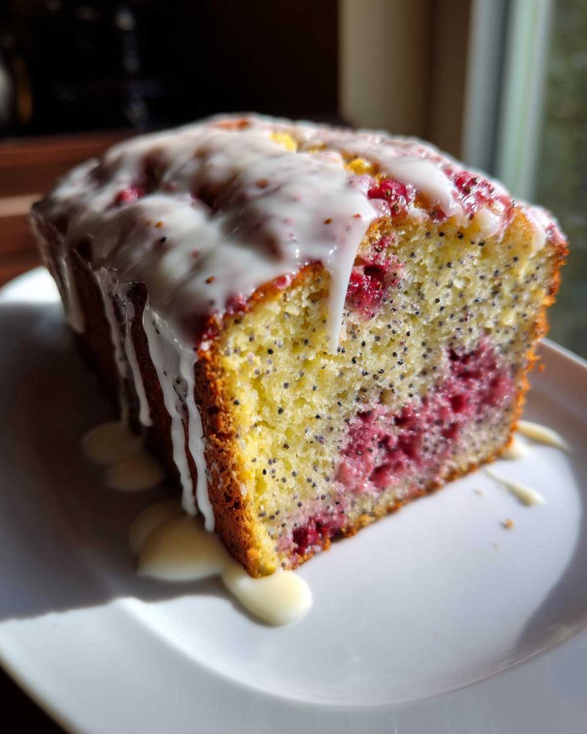 Close-up of a slice of Strawberry Lemon Poppyseed Loaf with bright pink berries and a thick white lemon glaze dripping down.