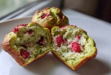 A Strawberry Matcha Yogurt Muffin cut in half showing the moist, green interior with visible pieces of strawberry.