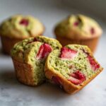 A Strawberry Matcha Yogurt Muffin cut in half showing the vibrant green matcha crumb and bright red strawberry pieces inside.