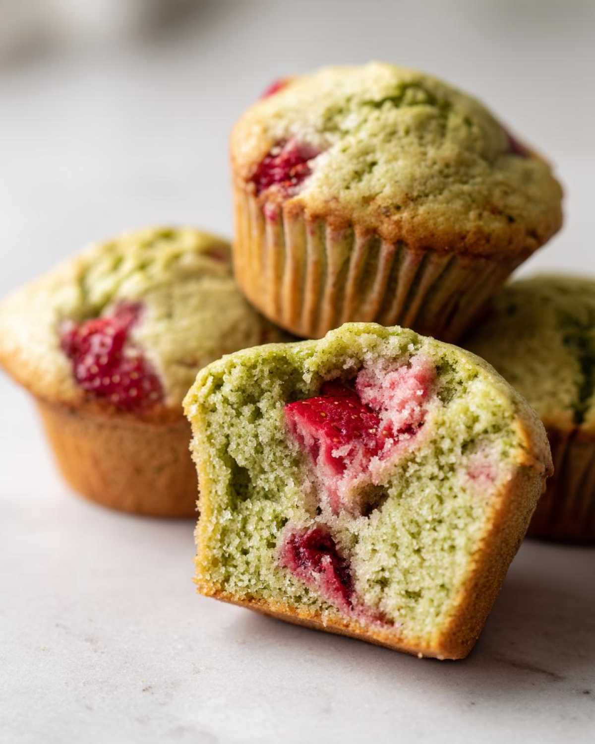 A close-up of a Strawberry Matcha Yogurt Muffin cut in half, showing the green matcha crumb and bright red strawberry pieces inside.