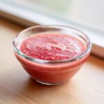 Close-up of freshly blended Strawberry Miso Vinaigrette, bright pink and slightly textured, in a small clear glass bowl.