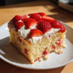 A tempting slice of Strawberry Vanilla Sheet Cake with fresh strawberries and cream on a white plate.
