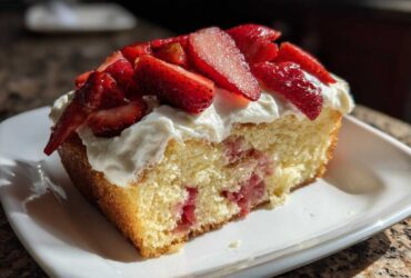 Close-up of a slice of moist Strawberry Vanilla Sheet Cake with fresh strawberries and whipped topping.