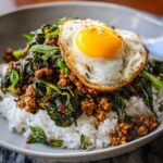 Close-up of Thai Basil Chicken Pad Krapow served over white rice, topped with a crispy fried egg.