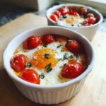 Close-up of a baked egg with a bright orange yolk, surrounded by roasted cherry tomatoes and fresh basil, part of the Tomato Basil Baked Eggs recipe.