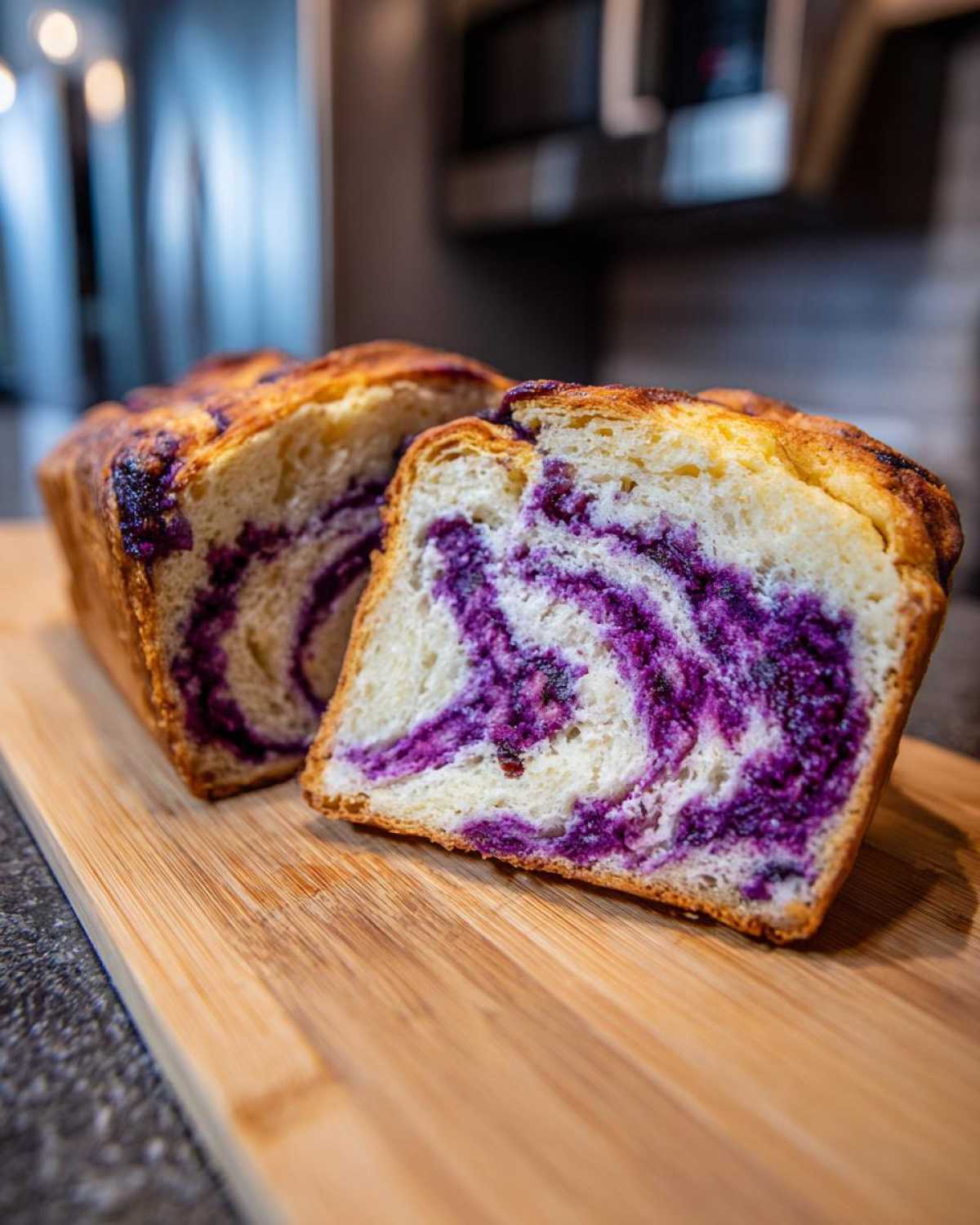 A loaf of Ube Coconut Swirl Bread sliced in half, showing the beautiful purple ube swirl filling inside the soft white bread.
