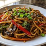 A close-up of a delicious Udon Stir-Fry with Sesame Vegetables, featuring thick noodles, broccoli, peppers, and mushrooms.