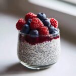 Close-up of Vanilla Berry Chia Pudding Cups layered with jam and topped generously with fresh raspberries and blueberries.