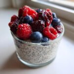 Close-up of a glass containing Vanilla Berry Chia Pudding Cups topped generously with fresh raspberries, blueberries, and blackberries.