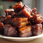 A close-up of glistening, dark brown cubes of Vietnamese Caramel Pork piled high on a white plate.
