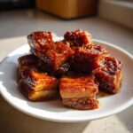 Close-up of glistening, caramelized pork belly cubes served on a white plate, showcasing the rich color of Vietnamese Caramel Pork.