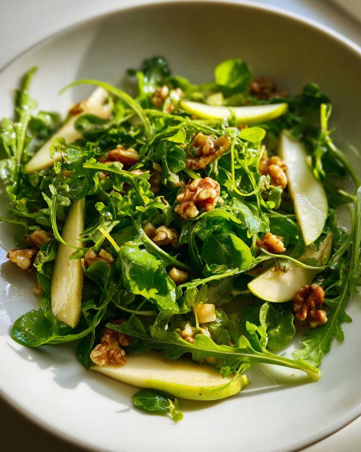 Close-up of a vibrant Watercress Apple Walnut Salad featuring bright green leaves, sliced green apples, and toasted walnuts.