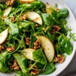 Close-up of a vibrant Watercress Apple Walnut Salad featuring glossy greens, thin apple slices, and crunchy walnuts.