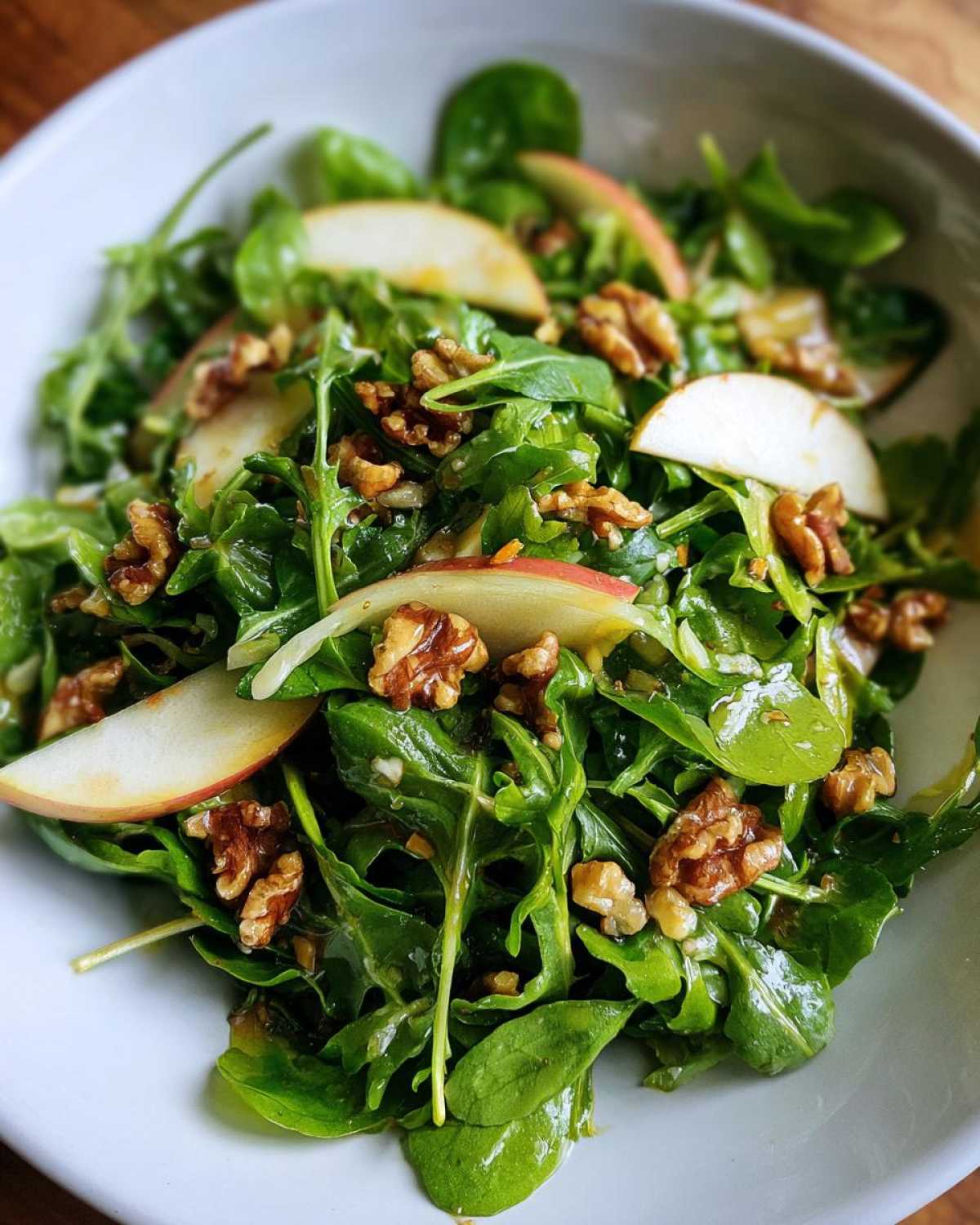 Close-up of a vibrant Watercress Apple Walnut Salad tossed in dressing, featuring green leaves, sliced apples, and toasted walnuts.