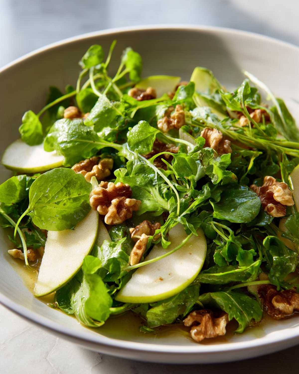 Close-up of a fresh Watercress Apple Walnut Salad tossed with dressing in a light-colored bowl.