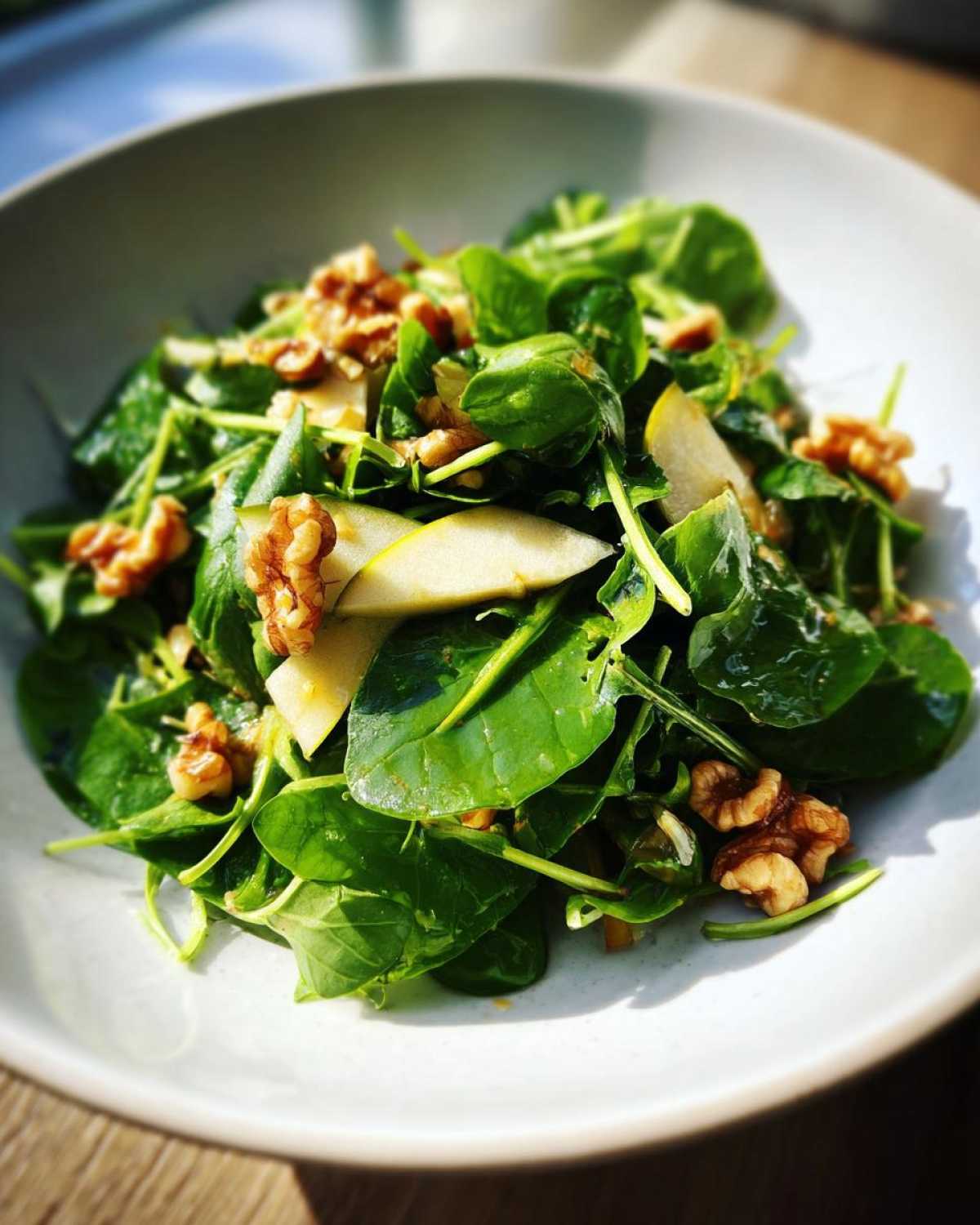 Close-up of a vibrant Watercress Apple Walnut Salad featuring dark green leaves, sliced apples, and whole walnuts in a light bowl.