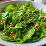 Close-up of a vibrant Watercress Apple Walnut Salad tossed with walnuts and sliced green apple in a white bowl.