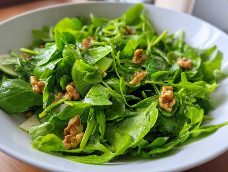 Close-up of a vibrant Watercress Apple Walnut Salad tossed with walnuts and sliced green apple in a white bowl.